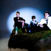 3 men posing on mossy rock with spotlight on them